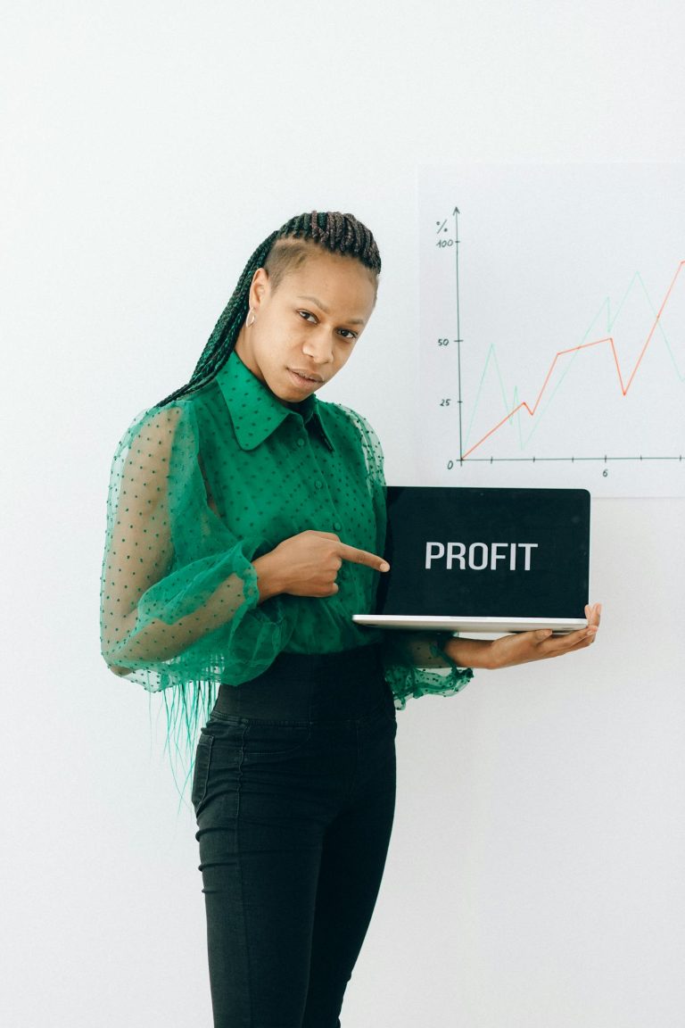 Confident businesswoman points at laptop displaying profit with growth chart in the background.