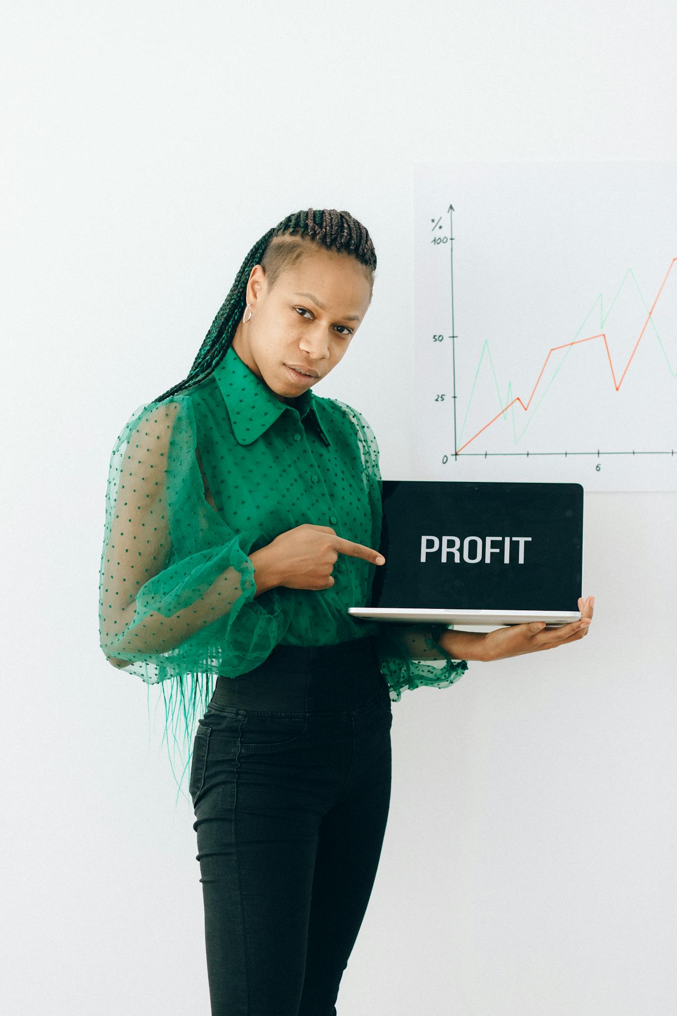 Confident businesswoman points at laptop displaying profit with growth chart in the background.